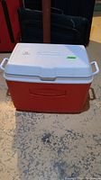 Front view of the Rubbermaid cooler with white lid and red base on concrete floor.