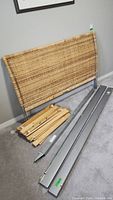 Disassembled bamboo headboard, metal side rails, and wooden slats placed on carpet.
