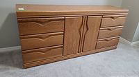 Front view of a laminate dresser showing wood grain finish, six drawers and a two-door cabinet center.