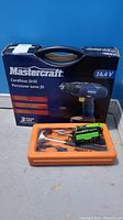 Mastercraft cordless drill in box and orange case with tools on floor