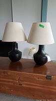 Two black Ikea table lamps with cream fabric shades on a wooden surface, showing full lamps and shades.