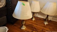 Three table lamps with metal bases and white lampshades sitting on a wood floor near a couch.