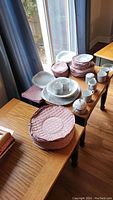 Overall view of all dishware including plates, bowls, coffee mugs, saucers, and serving items arranged on two tables.