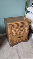 Front and side view of one vintage wood night table showing drawer design, metal handles, and some surface blemishes.