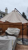 Patio umbrella open showing beige canopy and metal frame base blocks on wooden deck patio.