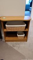 Frontal view of light wood laminate bookcase with two wicker baskets inside shelving compartments.