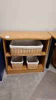Front view of laminate bookcase with three wicker baskets, one large and two smaller, on carpeted floor.