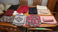 Overview of linens organized on table, showing various folded tablecloths, runners, and placemats in multiple colors and patterns.