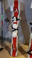 Full view of the red and white trick skis standing upright on a floor, with bindings and straps visible