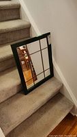 Framed mirror with black frame and multiple grid-pane mirror sections leaning on carpeted stairs