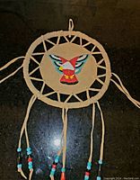 Front view of dream catcher showing tan leather hoop and leather strips forming web with beaded thunderbird in center and hanging strips with colorful beads.