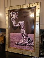 Front view of large framed giraffe photo with adult and calf touching noses, framed in wide textured light colored frame with gold inner border.