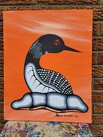 Front view of the original acrylic painting showing the loon against an orange background with rocks below and artist signature visible.