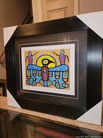 Frontal view of the professionally framed art print showing the black frame, matting, and colorful indigenous artwork.