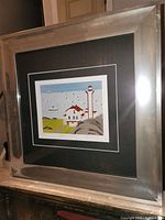 Image showing the full view of the silver framed Maud Lewis print titled 'Lighthouse and Ferry'.