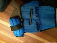 Photo showing two blue All Pro padded adjustable ankle weights, one folded and one open on wooden floor.