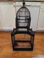 Front view of the antique French bird cage showing wooden base, metal wire cage, and dome top with hanging chain.
