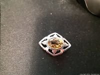 Close-up photo of the antique sterling silver brooch with the oval faceted amber-colored cairngorm stone in the center set in an openwork silver floral design.