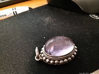Close-up of oval cabochon amethyst brooch detail showing color, silver beaded setting and bail.