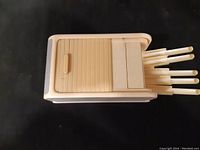 Top view of beige Bakelite cigarette dispenser with sliding lid and release levers extended.