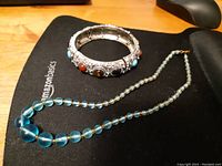Photo of the blue quartz bead necklace alongside the silver-tone bangle with decorative stones, set on a black AmazonBasics mat.