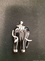 Front and side angle view of the black carved elephant pendant with silver-tone tusks, feet, and decorative metal adornments on the head.