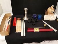 Photo showing multiple handmade beeswax candles in red, white, and tied red varieties, metal and votive candleholders, a brass snuffer, match bundle, and incense box.
