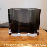 Front view of a thick smokey grey glass vase with a wavy rectangular shape on wooden surface.