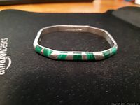 Side view of the silver bangle with green inlays showing the geometric shape