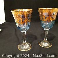 Two blue tinted wine glasses with clear stems, decorated with ornate gold etching around the rim and gold accented base.