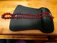 Full view of the vintage cherry amber bead necklace laid on a black case, showing the full length and color of the beads.