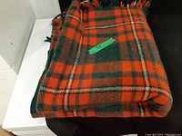 Folded tartan wool throw blanket with a red, green, and white plaid pattern, showing the edge and part of the folded body of the blanket.
