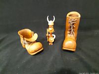 Photo of two carved wooden boots and MCM Danish Viking figurine on black background showing front and side views