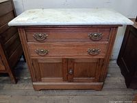Front view of antique wooden dresser with white marble top, showing 3 drawers and cabinet doors.