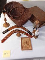 View of boomerangs, carved figurines, baskets, candle holder, carved ball, wooden box, and wooden artwork on a white cloth.
