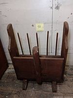 Front view of the wood cranberry scoop resting on a wooden floor, showing the wide base and central handle.