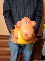 Front view of the orange and yellow rubber composite dinosaur sculpture, showing its large snout and eyes.