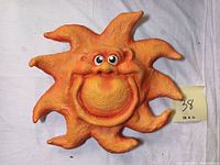 Front view of orange sun-shaped sculpture with a smiling face holding a sign showing dimensions 12 x 11 inches.