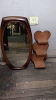 Photo showing the elongated oval wall mirror with a brown resin frame next to the heart-shaped wooden display shelf with three tiers.