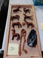 Photo showing all items in the set laid out in a wooden tray: seven wooden horse figurines, black hand sculpture, clay head, and clay skeleton figure.