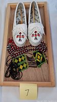Pair of white Minnetonka moccasins with thunderbird beadwork and two Indigenous beaded necklaces on wooden tray