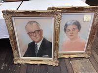 Two vintage pastel portraits in ornate gold frames, showing a seated man and woman.