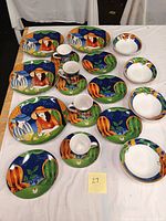 Full set of 19 Sango Paris Cafe patterned china pieces includes plates, mugs, saucers, and bowls arranged on white table showing colorful Parisian café themed illustrations.
