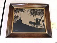 Framed colonial silhouette painting showing horse-drawn carriage and church steeple in silhouette form.