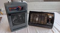Photo showing Honeywell Pro Series gray vertical space heater next to black Comfort Zone compact heater on table.