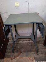 Front view of the green metal typewriter table with drop sides folded down showing tabletop and legs