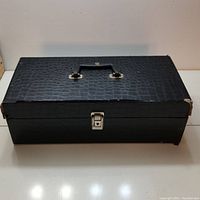 Closed black textured storage case with handle and metal latch