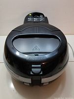 Closed top view showing black plastic air fryer with control buttons on top and viewing window in lid.