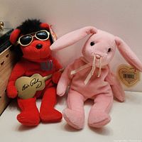 Two Ty Beanie Babies plush toys: Heartbear Hotel red bear with sunglasses and gold guitar, and Hoppity pink bunny with ribbon.