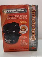 Front of boxed Proctor Silex breakfast sandwich maker showing product features and image of sandwich.